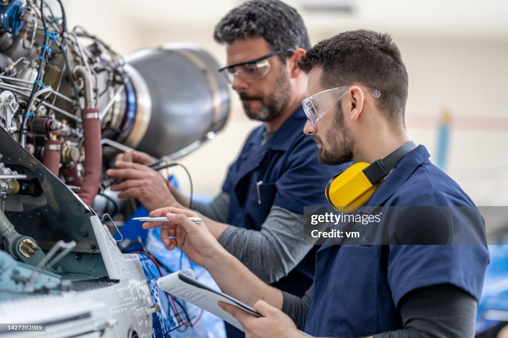 Mécaniciens d’aviation vérifiant le moteur de l’hélicoptère avec multimètre, vue latérale