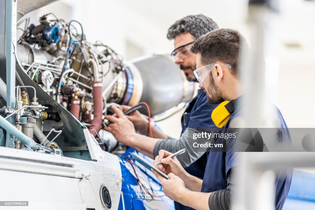 Mécaniciens d’aviation examinant le moteur avec multimètre, vue latérale