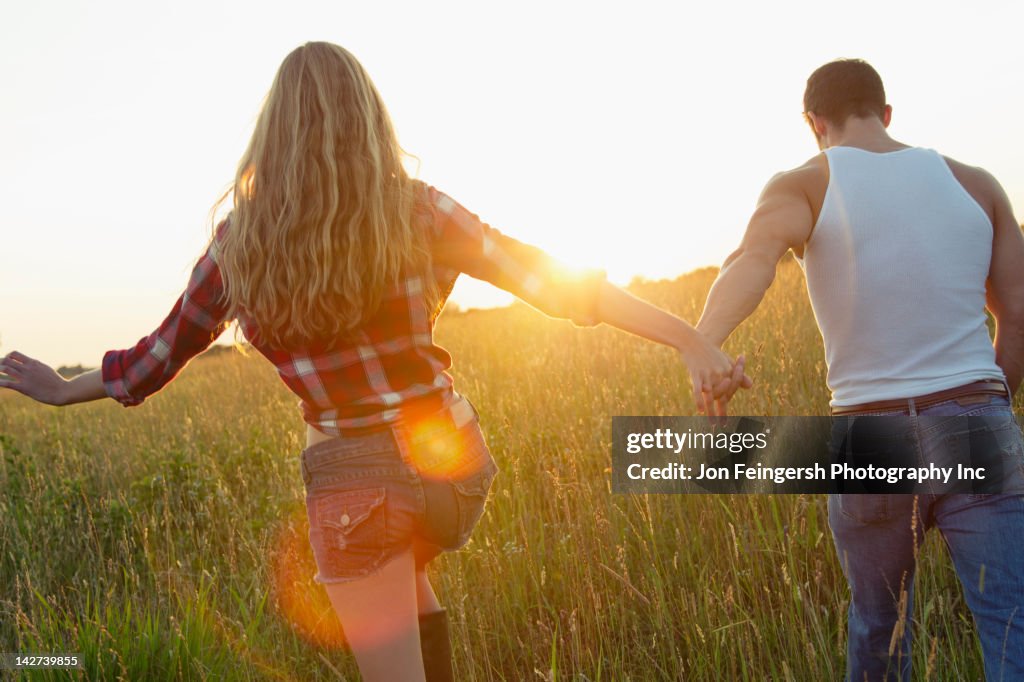 Caucasian couple walking in field holding hands