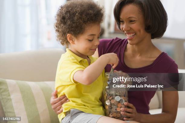 mother and son holding jar of coins - african american woman with money stock-fotos und bilder