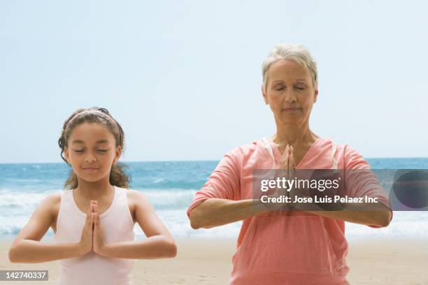 grandmother and granddaughter practicing yoga on beach - diferença entre gerações - fotografias e filmes do acervo