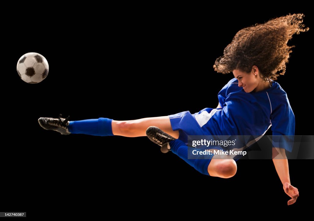 Caucasian soccer player kicking ball in mid-air