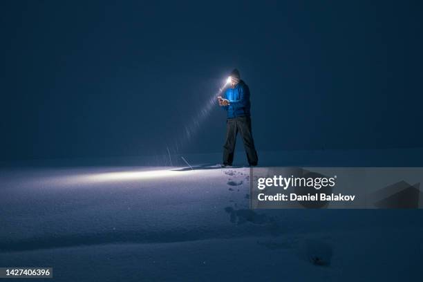 man in deep snow at night searching for the road on his phone. - winter_storm stock pictures, royalty-free photos & images