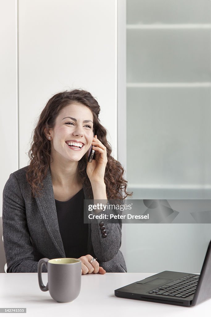 Businesswoman using cell phone at desk