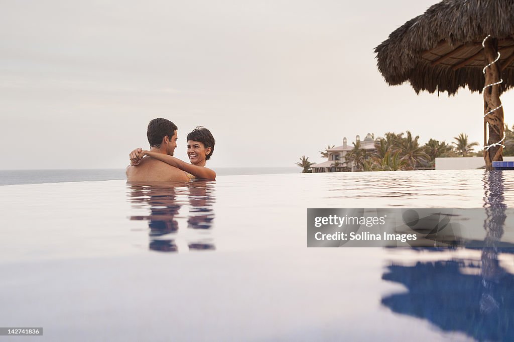 Hispanic couple hugging in swimming pool