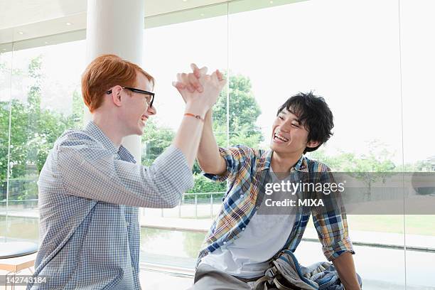 two young men clasping hands at campus - international student day stock-fotos und bilder