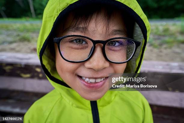 the boy is standing in the rain and there are drops on his glasses. - enjoy monsoon stock-fotos und bilder