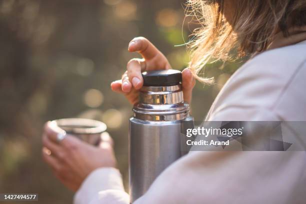 young woman pouring tea in a pine forest - flask stock pictures, royalty-free photos & images