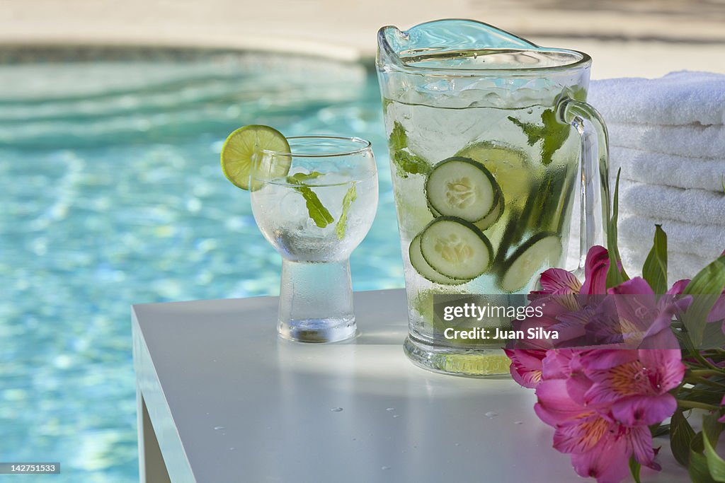 Pitcher and glass of water with cucumber by pool