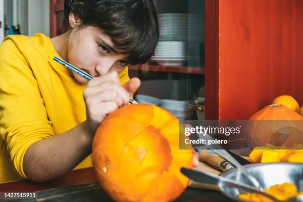 girl drawing face on halloween  pumpkin in kitchen - halloween stencil stock pictures, royalty-free photos & images