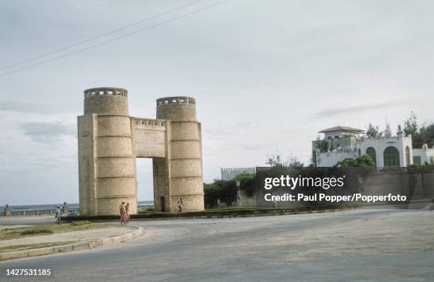 Pedestrians walk past the Arco del Re at the entrance to Corso Benito Mussolini near the port in Mogadishu, capital city of Somalia circa 1960. The...