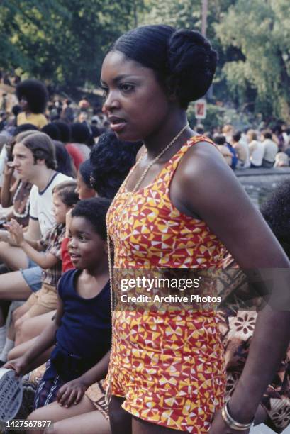 Young woman, wearing a yellow, red and white playsuit, possibly beside the fountain and pool in Washington Square Park, in the Manhattan borough of...
