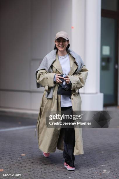 Maria Barteczko seen wearing a khaki green oversized trenchcoat by NA-KD, an ARKET wool sweater over the shoulders, a grey oversized ARKET sweater, a...