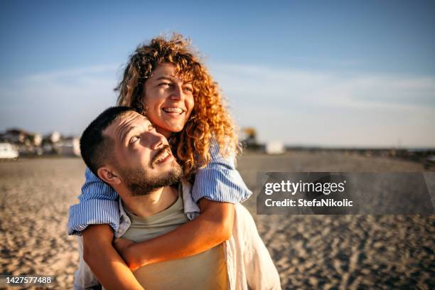 young couple at the beach at sunset - young couple on beach stock pictures, royalty-free photos & images