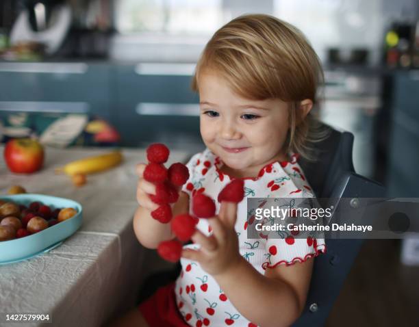 a baby girl playing with raspberries on her fingers, in the kitchen - sober leven stockfoto's en -beelden