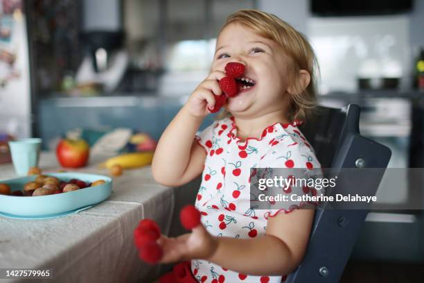 a baby girl playing with raspberries on her fingers, in the kitchen - children fruit stock-fotos und bilder