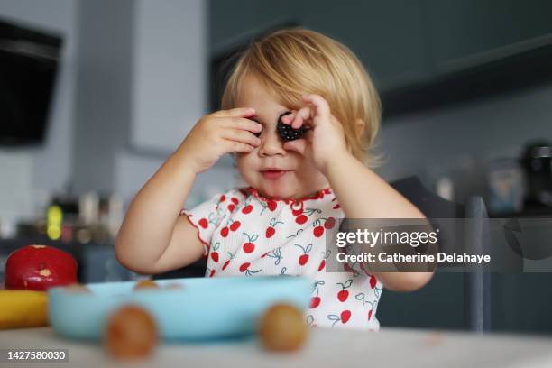 a baby girl playing with blackberries in the kitchen - baby spielt mit essen stock-fotos und bilder