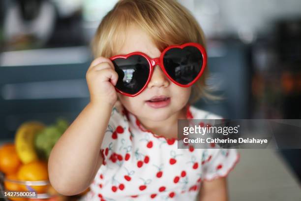 a 2 year old girl posing with a pair of heart-shaped glasses - baby sunglasses stock pictures, royalty-free photos & images