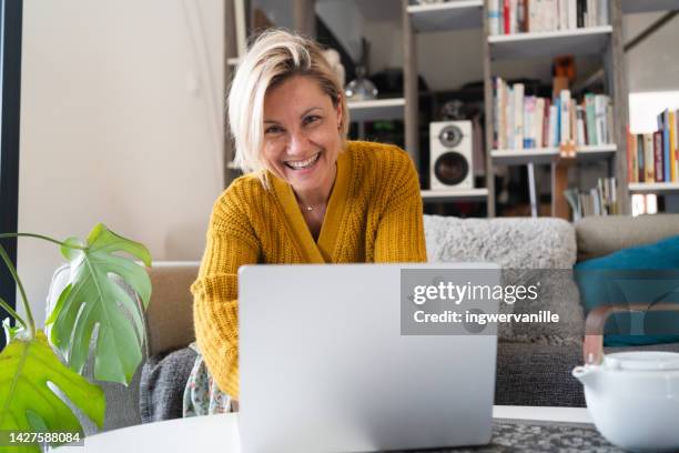smiling woman using laptop in living room - alleen één oudere vrouw stockfoto's en -beelden
