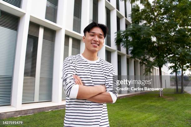 portrait photography of a young man from asia standing front of the camera with crossed arms. looking at camera with a smiley face. - nepalese ethnicity - fotografias e filmes do acervo