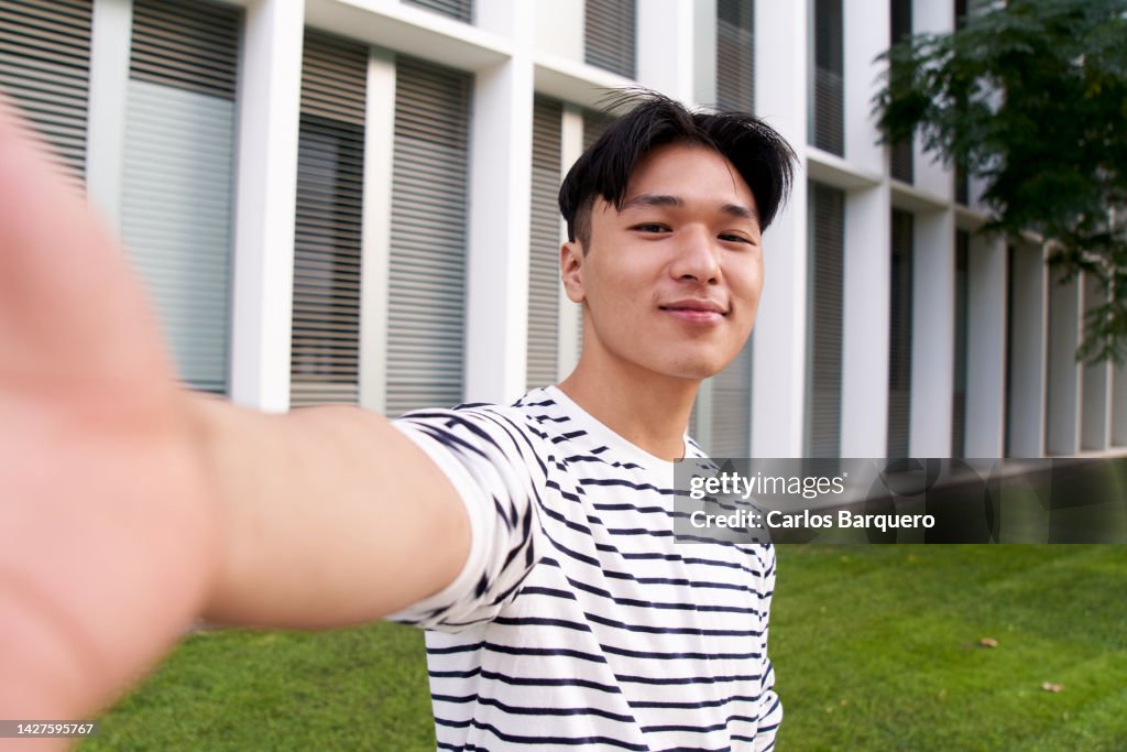 Cheerful asian man taking selfie of him with cellphone, outside campus university. Social media usage.