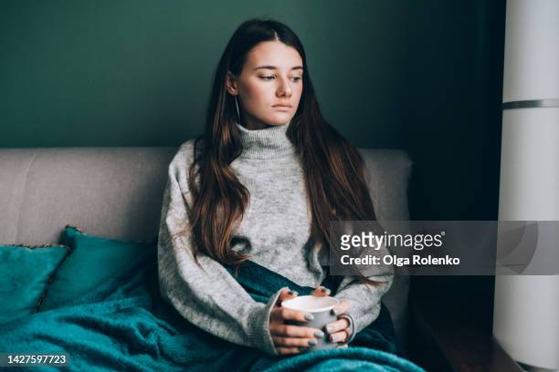 antioxidant vitamin hot drink. frost woman with hot drink trying to get warm, wrapped in a blanket in cold house - winter sofa stock pictures, royalty-free photos & images
