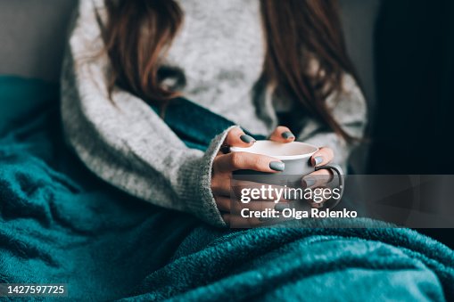 Cold loneliness in wet season. Cropped woman in warm clothes drink hot tea, wrapped in blanket Cold loneliness in wet season. Cropped woman in warm clothes drink hot tea, wrapped in blanket