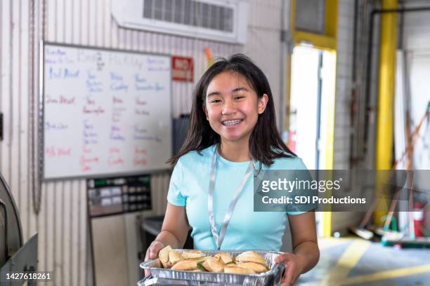 young teen volunteer holds tray of sandwiches at soup kitchen - selfless stockfoto's en -beelden