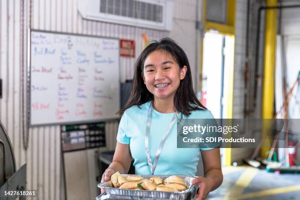 young teen volunteer holds tray of sandwiches at soup kitchen - altruismo stock pictures, royalty-free photos & images