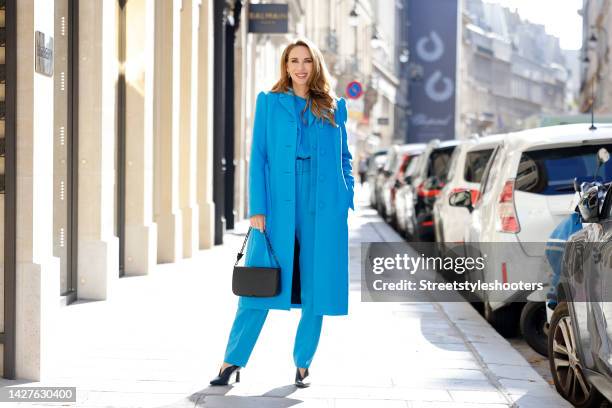 Alexandra Lapp wearing a blue silk top by Marc Cain, blue pants by Marc Cain, blue blazer by Marc Cain, blue coat by Marc Cain, a black bag by Marc...