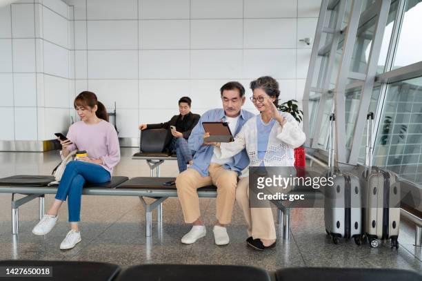 happy senior asian couple video call using digital tablet while waiting to board abroad for holiday vacation - kuala lumpur airport stockfoto's en -beelden