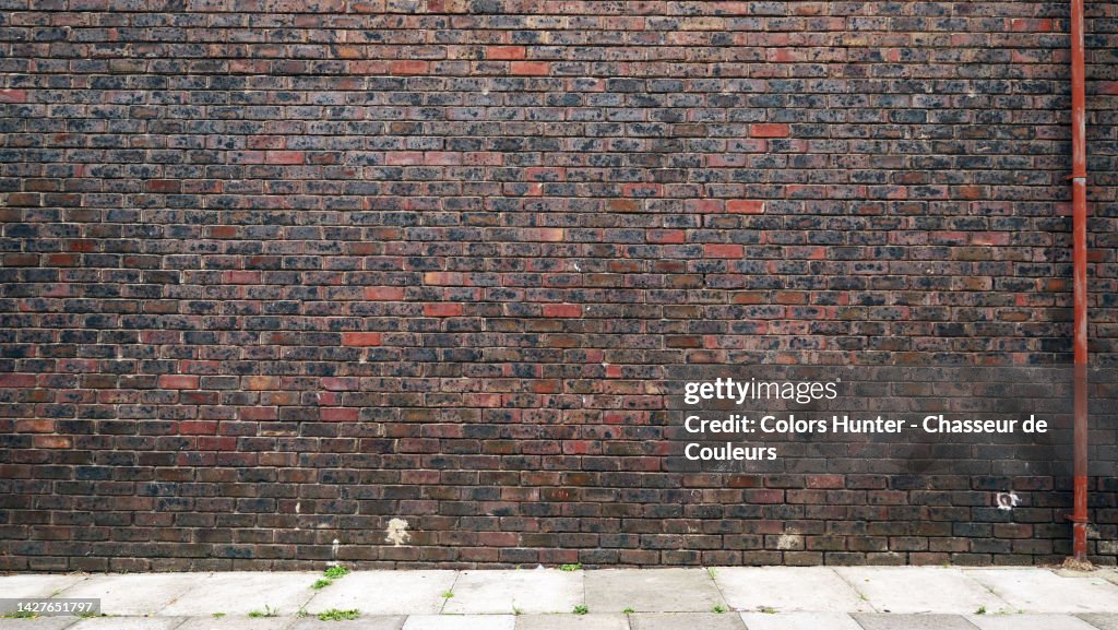 Empty dark brown brick wall with metal tube and cement slab sidewalk in London, England, UK