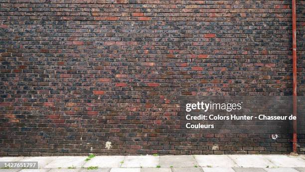 empty dark brown brick wall with metal tube and cement slab sidewalk in london, england, uk - bakstenen muur stockfoto's en -beelden