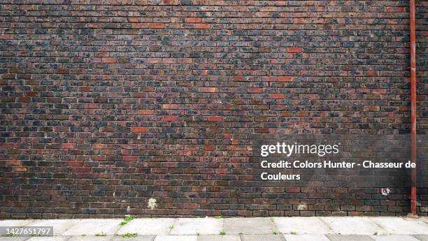 empty dark brown brick wall with metal tube and cement slab sidewalk in london, england, uk - brickwall stockfoto's en -beelden