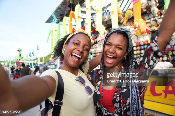 excited portrait of two black women at amusement park taking a selfie looking at camera with big smiles. - park festival bildbanksfoton och bilder