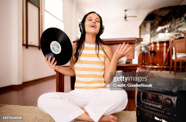 young woman listening to retro vinyl record from a music player at home - personal stereo stockfoto's en -beelden
