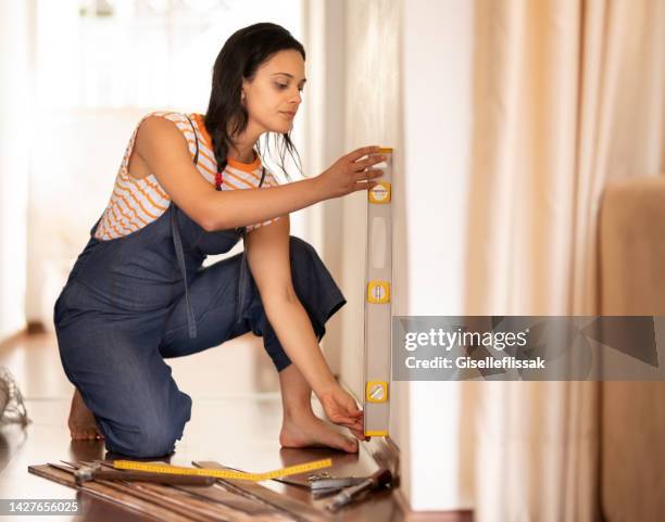 young woman using a level on wall while doing diy at home - waterpas stockfoto's en -beelden