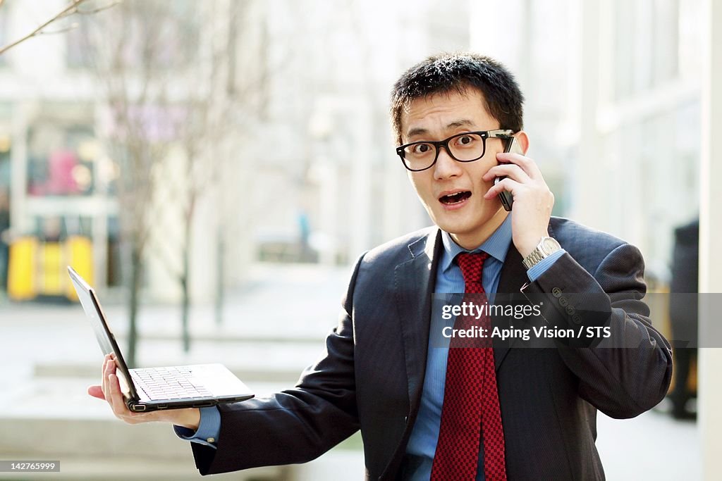 Businessman using mobile phone holding laptop