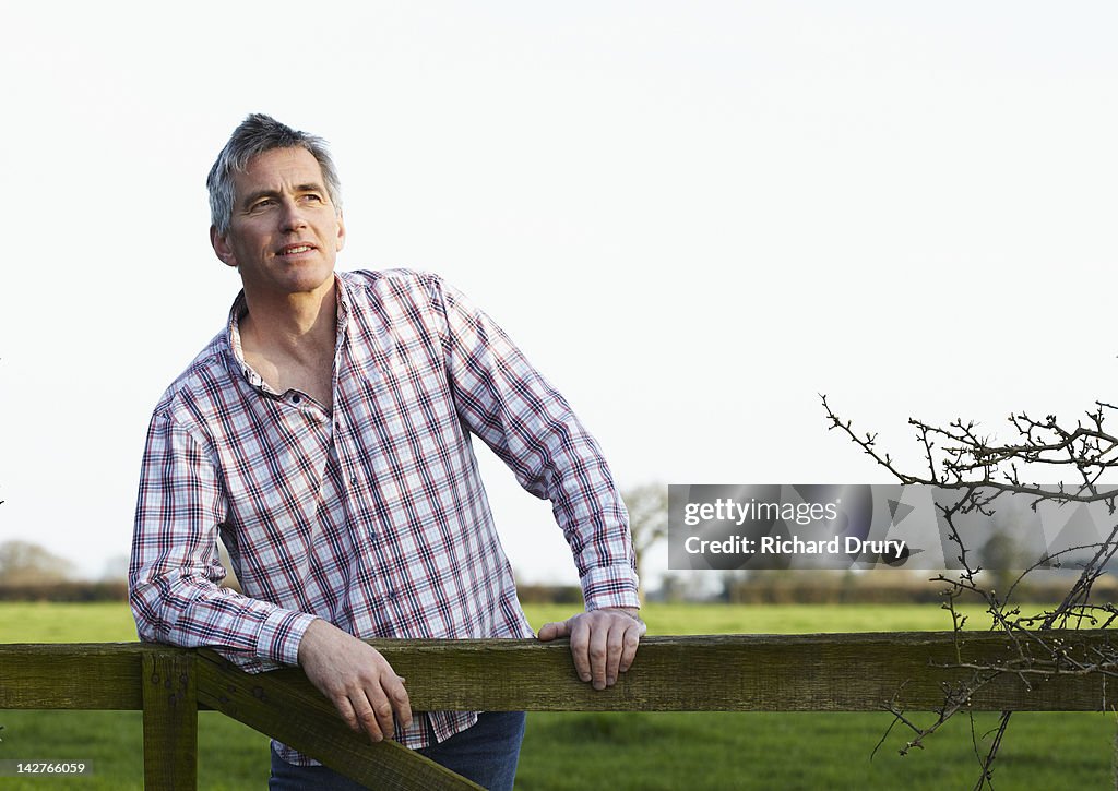 Mature man leaning on gate in countryside