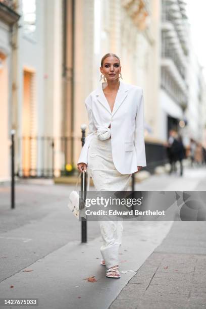 Leonie Hanne wears earrings, a white oversize cropped blazer jacket with a knot, a white skirt with knitted patterns, a white Jacquemus bag, shoes,...