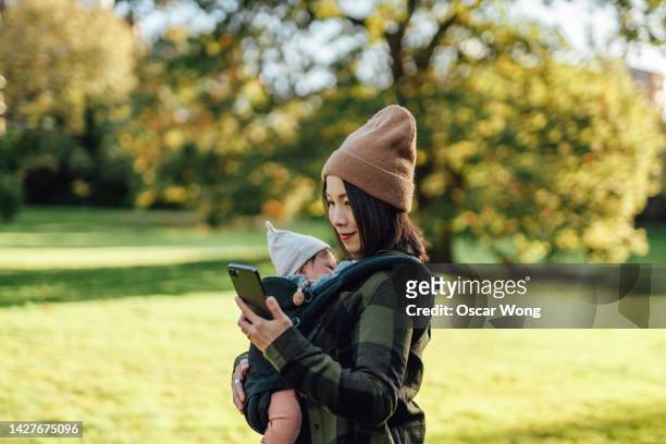 young asian mother using smart phone while having a walking with her baby in the park - country stock photos et images de collection