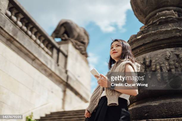 young asian woman using smart phone while traveling in europe - ローアングル 女性 ストックフォトと画像
