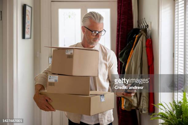 man receiving a package at home and getting a notification on his cell phone - notification stock pictures, royalty-free photos & images