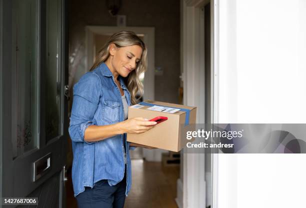 woman receiving a package at home and getting a notification on her cell phone - receiving delivery stock pictures, royalty-free photos & images