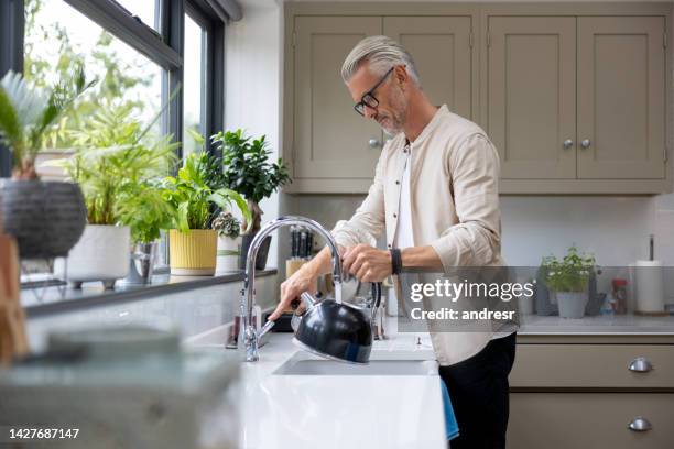 man makign a cup of tea and putting the kettle on - caldeira imagens e fotografias de stock