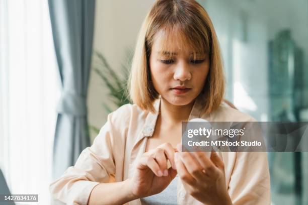 young woman hold medicine searching information online by laptop in living room at home. - prescription label stock pictures, royalty-free photos & images