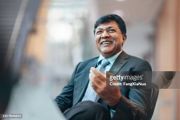 asian indian mature businessman talking and laughing with colleague during meeting in business office wearing suit - business man sitting banking imagens e fotografias de stock