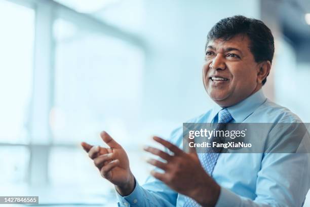 asian indian mature businessman talking discussion smiling laughing in meeting gesturing hands in bright business office - entrevista imagens e fotografias de stock