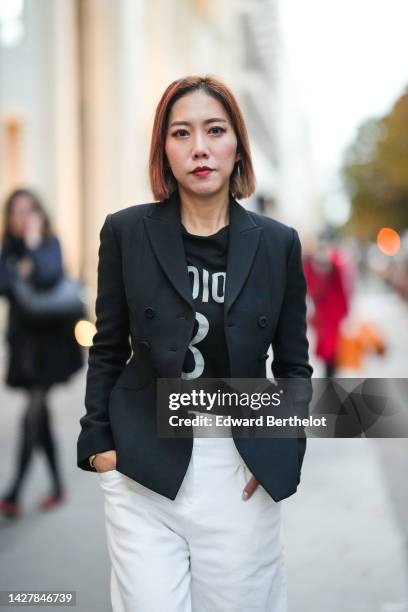 Guest wears a black blazer jacket, a black with white print pattern t-shirt from Dior, white large pants, outside Jacquemus, during Paris Fashion...