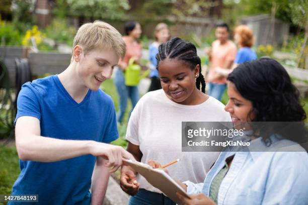 diverse multiracial group of young volunteers coordinate plans together with mature project manager at community garden park in neighborhood environment - inclusive leadership stock pictures, royalty-free photos & images
